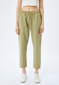 Pantalons légers verts clair, à coupe décontractée, avec une taille élastique, un cordon de serrage, deux poches latérales et des ourlets effilochés. Le matériau semble doux et durable.