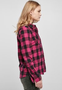Chemise à carreaux rose et noire avec des manches longues, un col et deux poches poitrine. Fabriquée en tissu doux avec une coupe décontractée.