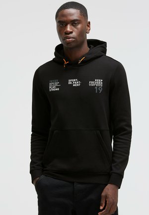 Black hooded sweatshirt with orange drawstrings. Features printed text in white and gray across the front. Includes a front kangaroo pocket.