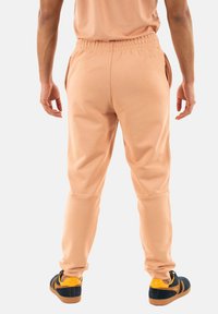Joggers de melocotón con cinturilla elástica y bolsillos laterales, hechos de una suave tela, diseño de pierna ajustada, combinados con zapatos negros y amarillos.