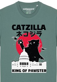 T-shirt en coton vert menthe avec un graphisme d'un chat noir, un cercle rouge et une silhouette blanche d'un bâtiment, avec du texte au-dessus et en dessous.