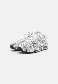 White sneakers with a black cartoon-style graphic pattern. Features a textured sole and classic lace-up design. Accented with subtle branding.