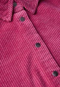 Camicia di velluto a coste fucsia con un motivo a texture, dotata di un colletto e di bottoni a pressione in metallo nero lungo la parte anteriore.