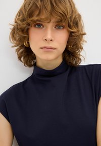 Laadukkaasta pehmeästä kankaasta valmistettu tummansininen mock neck -paita, jossa on lyhyet hihat ja sileä pinta. Minimalistinen muotoilu ilman kuvioita tai koristeita.