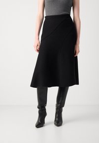 Black wool skirt with a flared design and diagonal seams, paired with fitted black leather knee-high boots. Smooth texture with subtle detail.