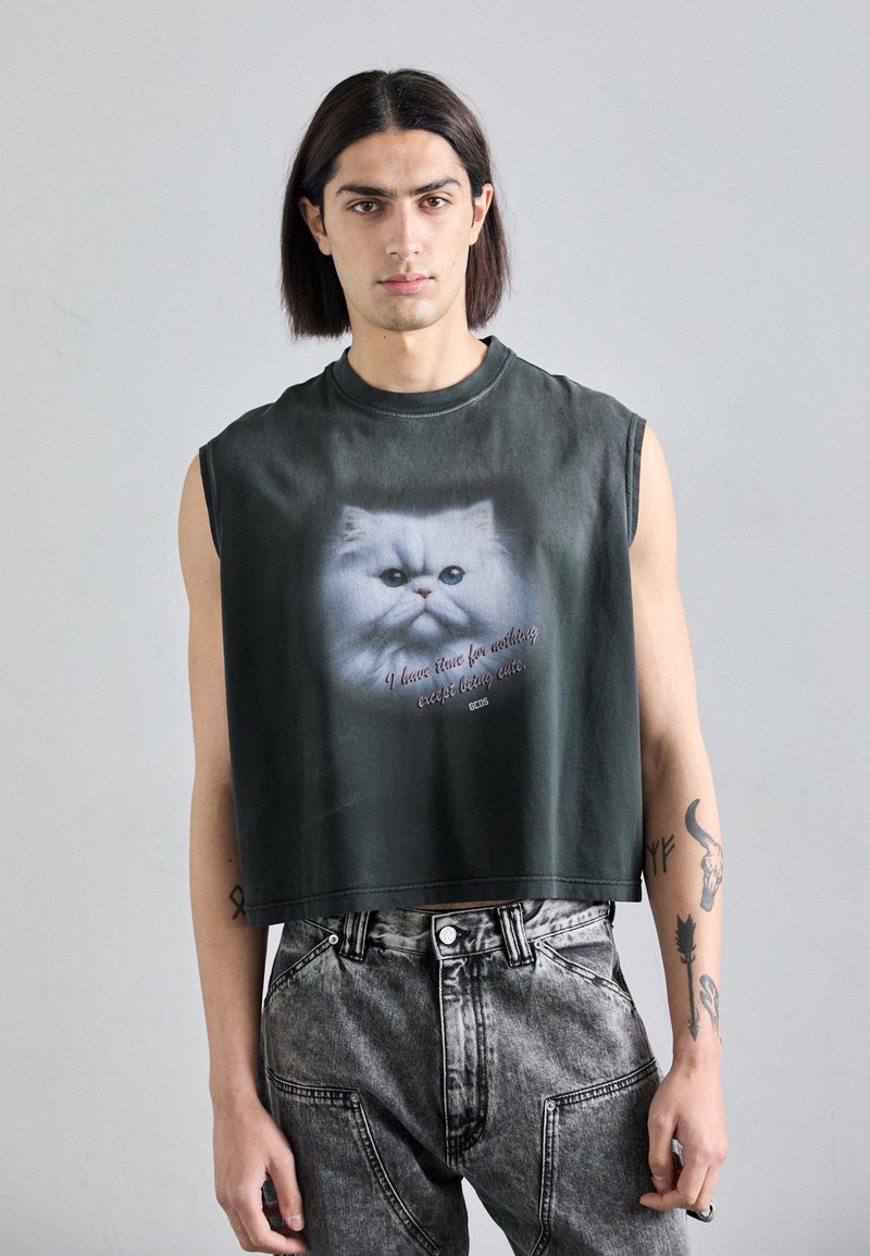 Black cropped sleeveless shirt featuring a large printed image of a white cat with blue eyes and text below. Worn with gray distressed jeans.