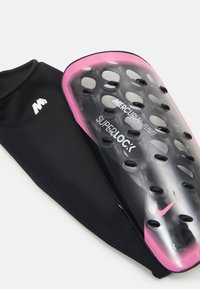 Il parastinchi Nike Mercurial Superlock presenta un guscio in plastica trasparente con dettagli rosa, fori di ventilazione e una manica in tessuto nero con il logo.