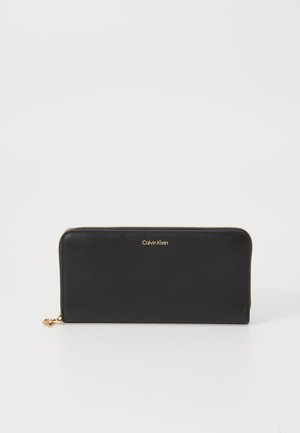 Black leather wallet with gold hardware, zip closure, and embossed logo. Features a sleek rectangular shape and a smooth texture.