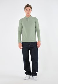 Langærmet, lys grøn polo-shirt med krave og tre knapper, parret med mørkeblå jeans og hvide sneakers.