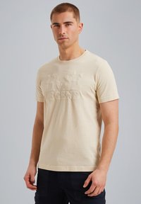 Beige puuvillapaita lyhyillä hihoilla. Edessä kohoava teksti "LIVE LEGEND". Klassinen pyöreä kaula-aukko ilman graafisia elementtejä.