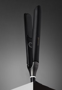 Fer à lisser noir au design élégant et plat, avec un bouton d'alimentation et des accents de logo. Câble attaché à la base pour une utilisation.