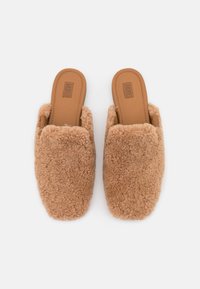 Karamelkleurige schapenvacht muiltjeslippers met een zachte, fluffy textuur en een open achterkant. Voorzien van een gladde bruine binnenzool en een rond design van de teen.