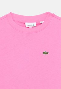 Ροζ βαμβακερό μπλουζάκι με στρογγυλή λαιμόκοψη, κοντά μανίκια και μικρό πράσινο κεντημένο λογότυπο κροκόδειλου στο στήθος.