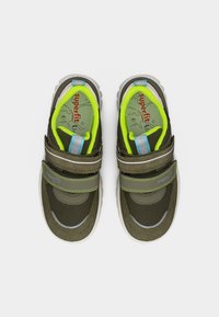 Ζευγάρι παιδικών αθλητικών παπουτσιών σε χρώμα ελιάς με φωσφορίζουσα κίτρινη επένδυση, ιμάντες με βέλκρο και λευκές σόλες, από πάνω σε λευκό φόντο.