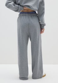 Grijze joggingbroek met een relaxte pasvorm, voorzien van een elastische tailleband met blauwe strepen. Gemaakt van zacht materiaal met een gladde textuur.