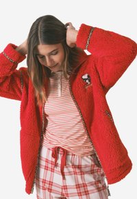 Czerwona polarowa kurtka z akcentami w leoparda, z zamykanymi kieszeniami i haftem Snoopy. Warstwowo nałożona z koszulą w paski i spodnimi piżamowymi w kratę.