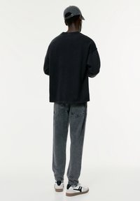 Sweatshirt noir oversized, pantalon en denim gris avec texture décolorée, et baskets blanches avec accents noirs, vues de dos.