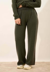 Ciemnozielone szerokie spodnie z miękkiego materiału, z plisowanym przodem i elastycznym paskiem w talii. W zestawie z jasnymi trampkami.