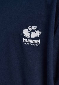 Hvid grafik af to fodboldstøvler, der skåler med glas trofæer over teksten "hummel SPORTSWEAR" på marineblåt stof.