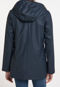 Veste imperméable marine avec capuche, présentant une texture lisse et élégante, des fermetures éclair et des accents discrets de quincaillerie jaune.
