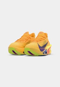 A Nike sportcipő élénk sárga kötött felsőrésszel rendelkezik, lila részletekkel és texturált talppal. A sarok jellegzetes színátmenettel bír.