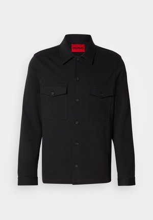 Black shirt jacket with long sleeves, button front, two chest pockets, and embroidered 'HUGO' logo in a textured fabric. Red interior label.