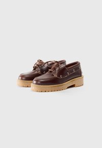 Zapatos de cuero marrón con punta redondeada, diseño de cordones y una suela de goma gruesa y texturizada que presenta un patrón de banda de rodadura visible.
