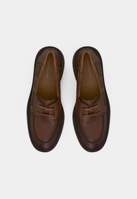 Καφέ δερμάτινα σκαφοπαπούτσια με στρογγυλή μύτη, λουριά με δύο μάτια και αντίθετη καουτσούκ σόλα. Ομαλή υφή και λεπτομέρειες ραφής ορατές.