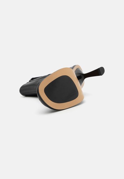 Svart sko med en rundad design, med en slät yta och en kontrasterande tanfärgad detalj på sulan. Snygg, modern estetik.