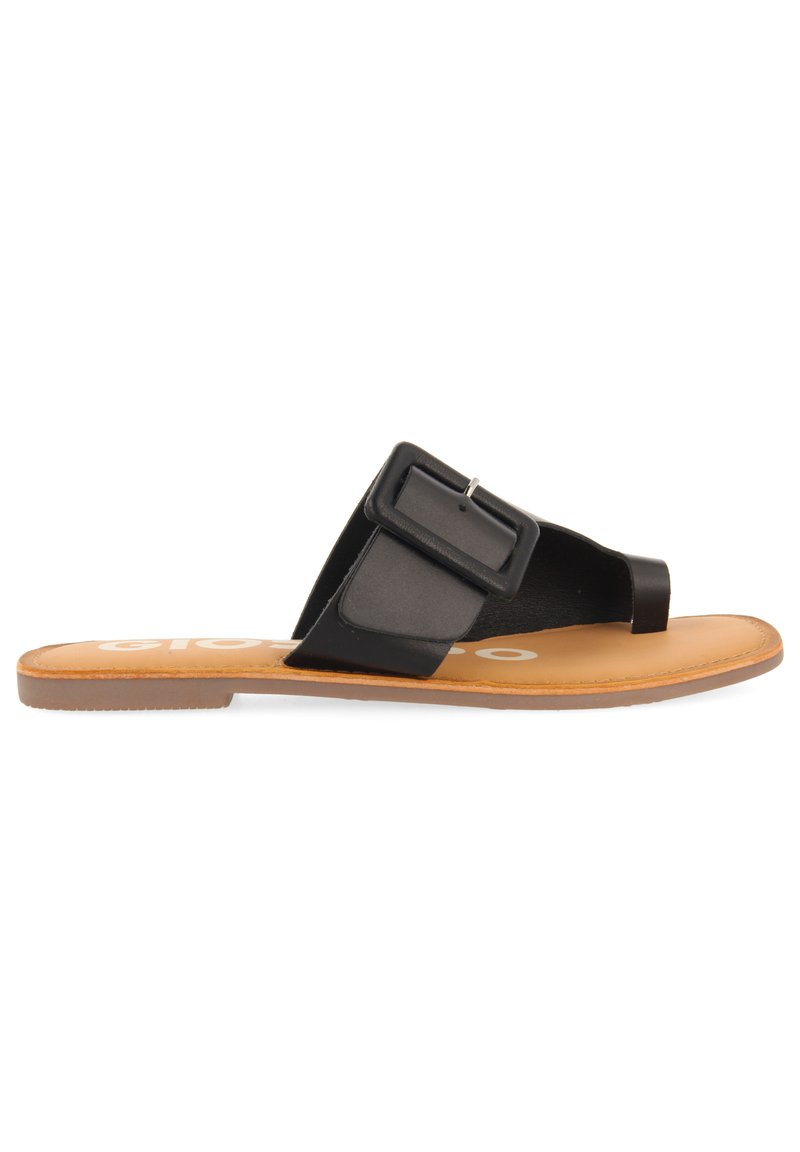 Des sandales plates noires présentent une large sangle avec une boucle carrée, une semelle intérieure couleur tan et une semelle en caoutchouc texturée. Le design est minimaliste et moderne.