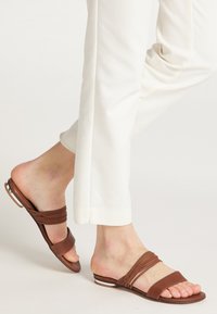 Bruine leren slipper sandalen met twee gevlochten bandjes, open teenontwerp en een platte zool met een subtiele witte accent.