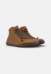 Zapatos altos marrones con cordones marrones y una suela texturizada, exhibidos sobre un fondo liso, destacando su diseño y material.
