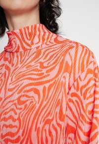 Gros plan d'une personne portant un haut à col roulé côtelé avec des rayures abstraites de zèbre aux couleurs vives orange et rose.