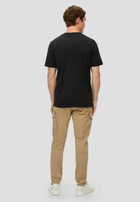 Schwarzes Baumwoll-T-Shirt mit Rundhalsausschnitt, Rückansicht. Kombiniert mit hellbeigen Cargo-Hosen, die seitliche Taschen und ein tailliertes Design aufweisen.