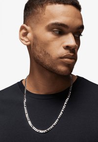 Silver chain necklace on a person wearing a plain black t-shirt. The necklace features interlocking links with a polished finish.