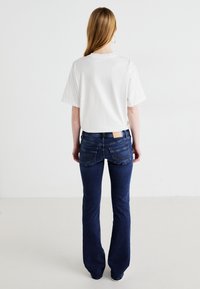 T-shirt en coton blanc à manches courtes associé à un jean en denim bleu foncé évasé avec des poches cousues et une étiquette marron clair sur la ceinture.