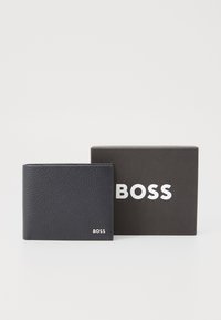 Crna kožna novčanica s teksturiranim završetkom i srebrnim logotipom "BOSS". Dolazi u crnoj kutiji s bijelim "BOSS" brendingom.