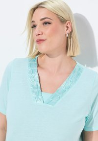 Una t-shirt azzurro chiaro con design a V presenta una rifinitura in satin lungo il collo. Il tessuto sembra morbido con maniche corte.