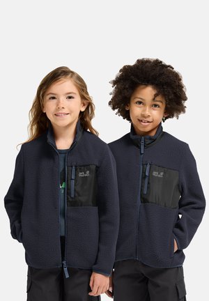Due bambini indossano giacche in pile blu navy con tasche pettorali nere con zip, in piedi fianco a fianco sorridenti contro uno sfondo neutro.