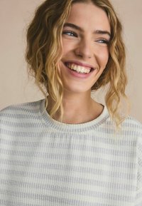 Light gray and white striped sweatshirt with a ribbed texture and round neckline. The fabric appears soft and relaxed fitting.