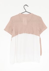 Helles rosa T-Shirt mit kurzen Ärmeln, das ein strukturiertes Oberteil aus Strick und ein glattes weißes Unterteil aufweist, hängt an einem schwarzen Haken vor einem weißen Hintergrund.