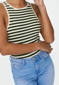 Top a righe verdi e bianche con lavorazione a costine e scollatura alta, abbinato a jeans in denim azzurro chiaro. Nessun logo o motivo visibile nel tessuto.