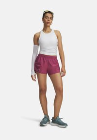 Enganliegendes weißes Tanktop, lila Sportshorts und türkise Sneakers. Die Shorts verfügen über einen elastischen Bund und Seitenschlitze für bessere Beweglichkeit.