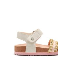 Sandalo bianco in suede con suola rosa e marrone, caratterizzato da un accento intrecciato in oro e una tracolla regolabile. Base testurizzata per una migliore presa.