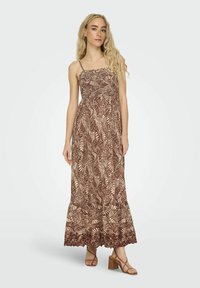 Robe maxi avec un motif de feuilles brun et crème, dotée de bretelles spaghetti ajustables et d'un corsage smocké. Jupe fluide avec bord en dentelle.