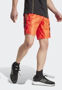 Lyse orange atletikshorts med et struktureret mønster, prydet med sorte sidelommer og detaljer. Båret med sorte sneakers og korte sokker.