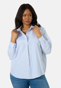 Camicia button-up a righe blu chiaro con colletto, maniche lunghe e vestibilità rilassata, abbinata a jeans blu. Tessuto testurizzato, design informale.