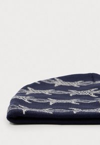 Hajlított sötétkék kötött sapka világosszürke tövisdrót mintával sima fehér háttéren.