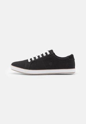Black canvas sneakers with white laces, round toe, padded collar, and contrasting white sole. Features logo on side and textured rubber outsole.
