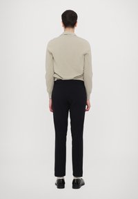 Lys grå langærmet skjorte parret med mørkeblå bukser, der har et tætsiddende design og subtile syninger. Sat mod en ensfarvet baggrund.